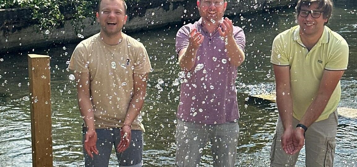 Drei Männer in einer Naturkneipanlage im Wasser stehend mit hochgekrempelten Hosen
