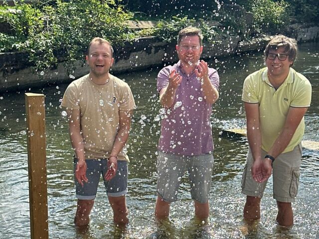 Drei Männer in einer Naturkneipanlage im Wasser stehend mit hochgekrempelten Hosen